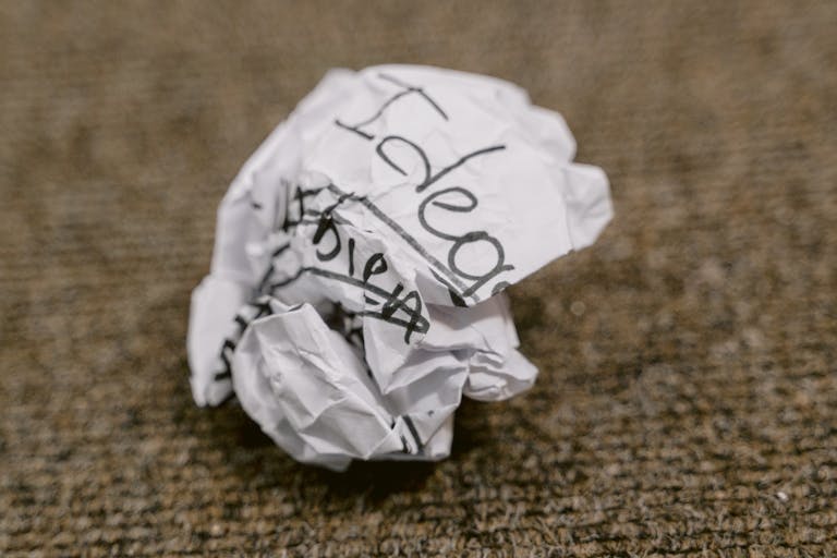 Close-up of a crumpled paper ball with 'Ideas' written on it, symbolizing discarded thoughts.