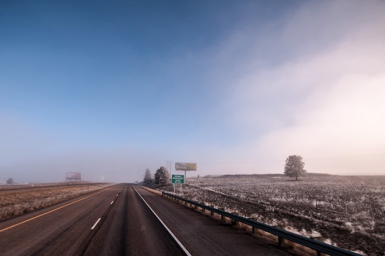 A scenic view of an open highway cutting through a foggy rural landscape under a clear blue sky.