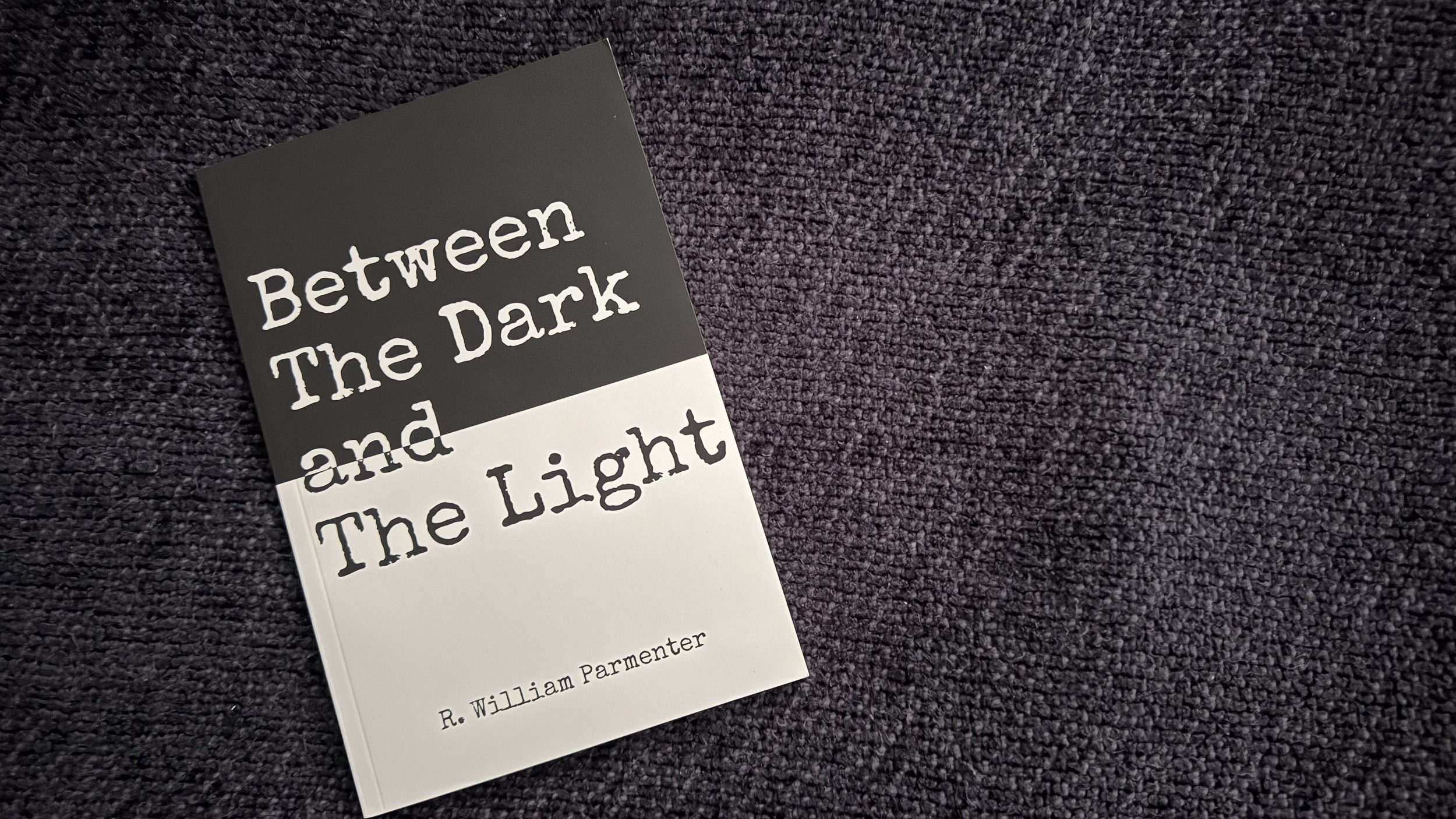 The book title Between The Dark and The Light sits on a dark, violet blanket.