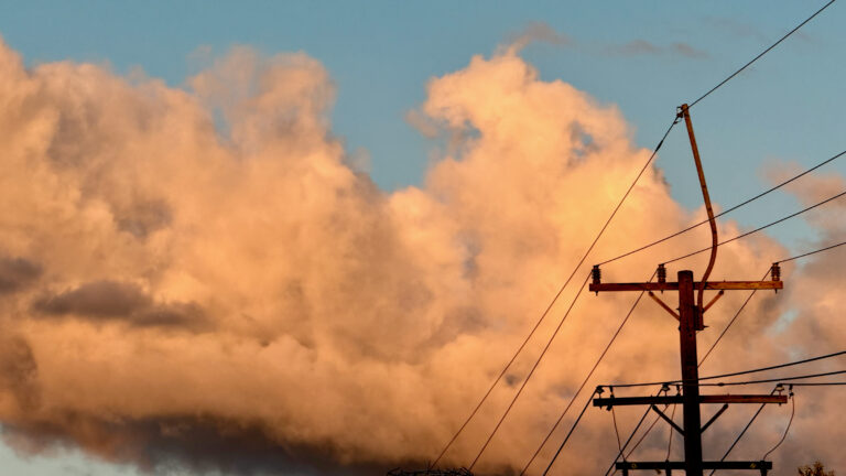 Clouds at sunset alight in orange against a blue sky. Power lines and a power pole take up a corner of the image.
