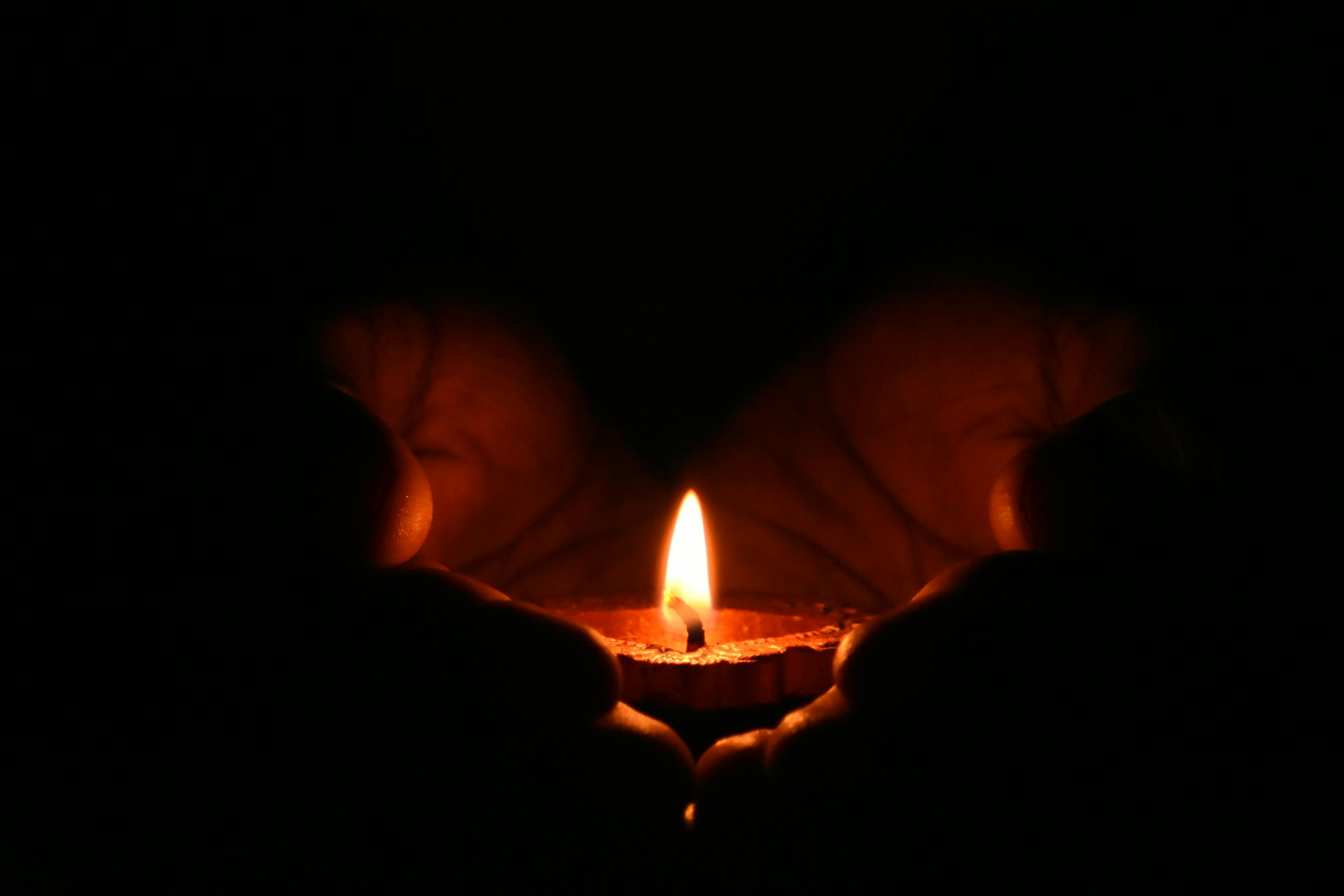 Close-up of hands embracing a lit candle in the dark.