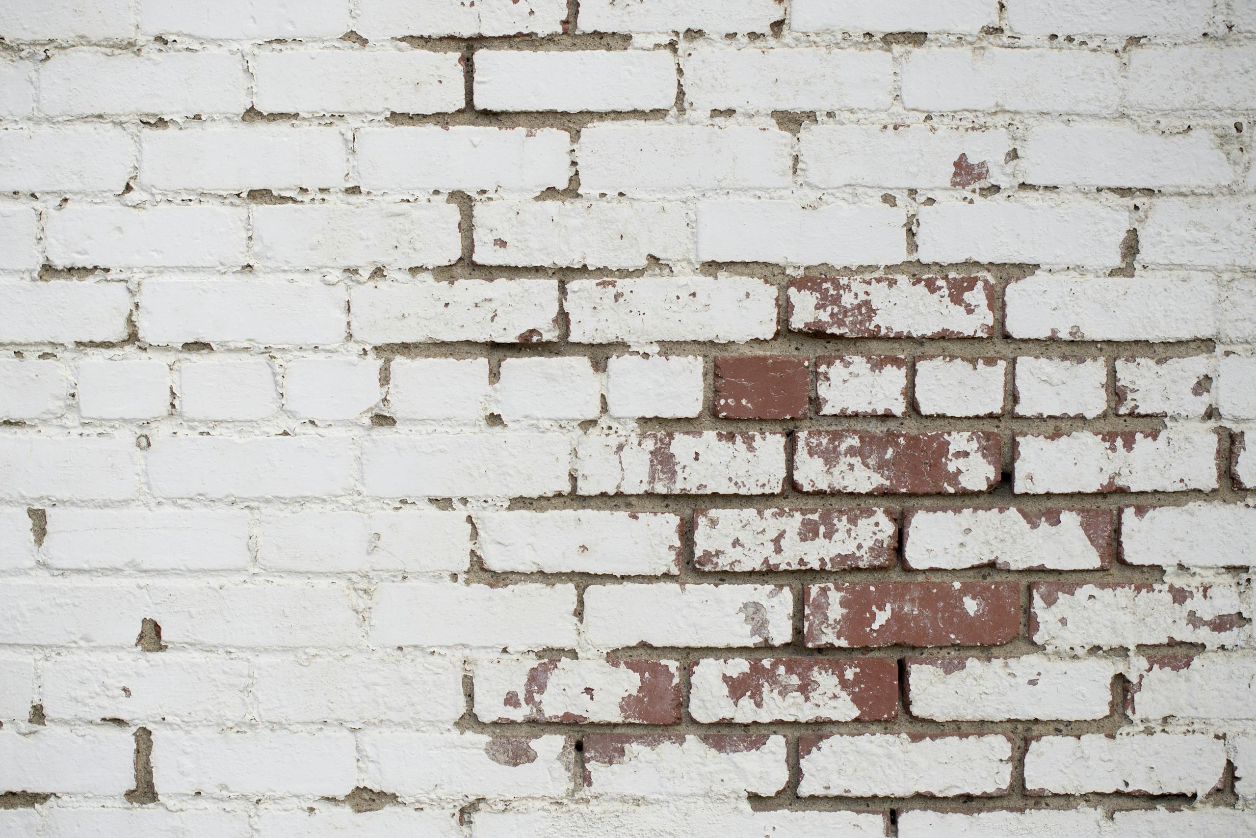Detailed texture of an old white brick wall with peeling paint and visible wear.
